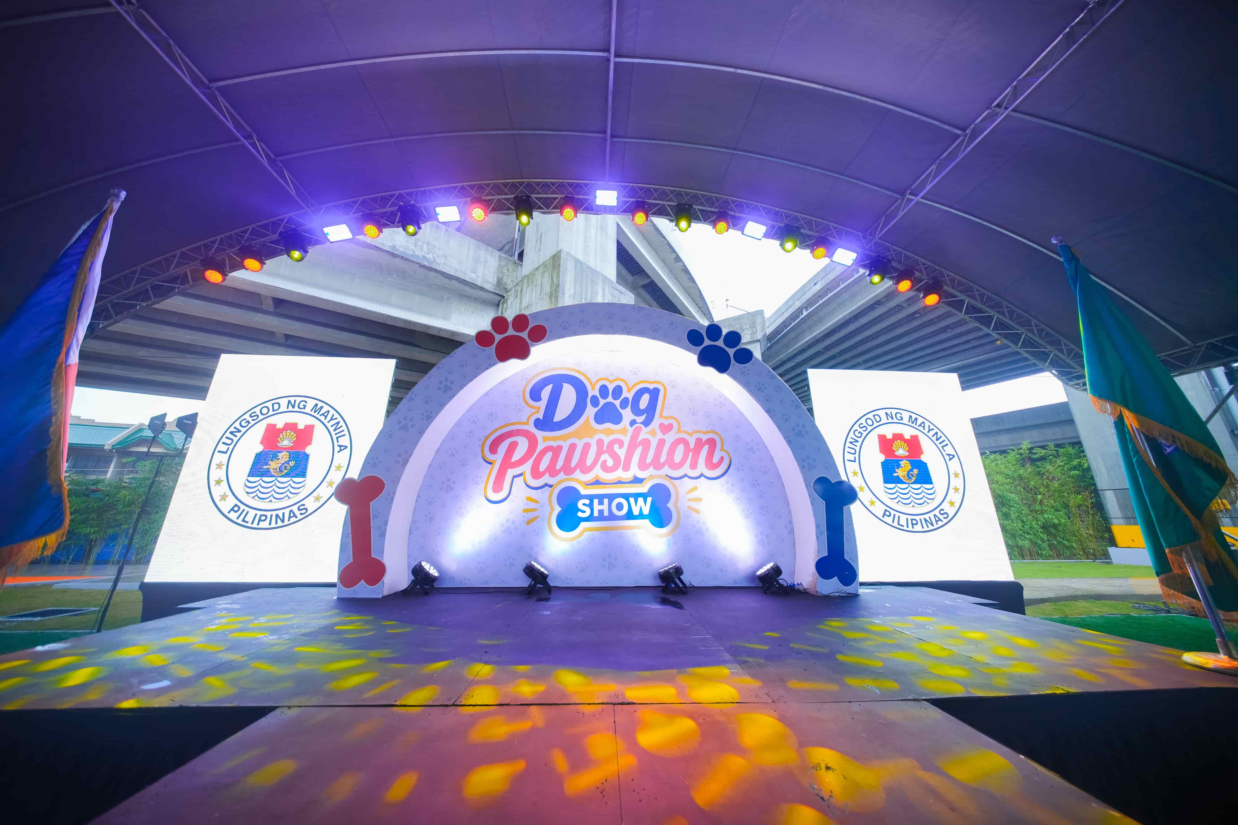 Arched Dog Pawshion Show stage under a covered court, with truss lighting and city seals